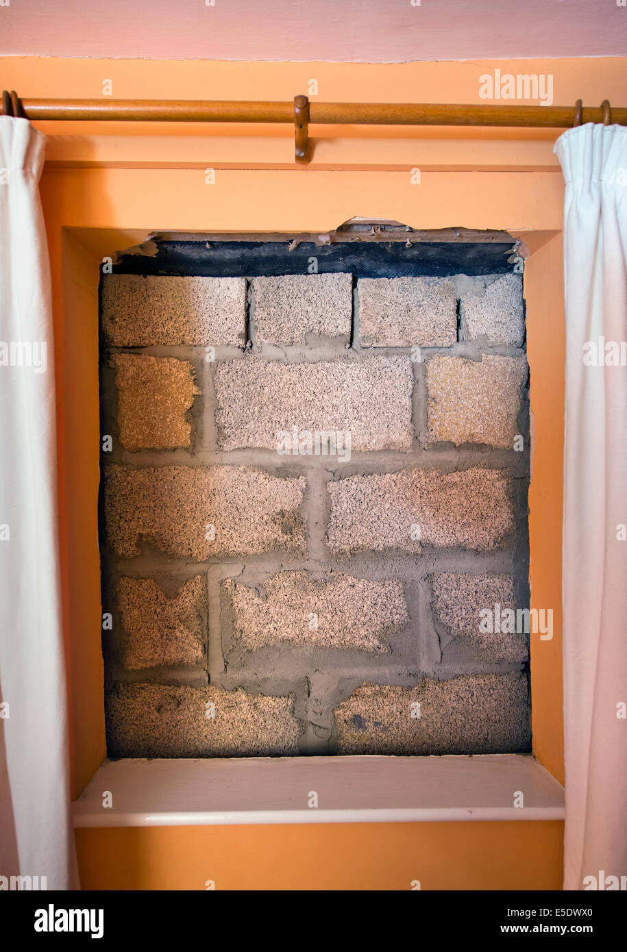 Una finestra murata con blocchi in calcestruzzo con camera da letto tende ancora appeso Foto Stock