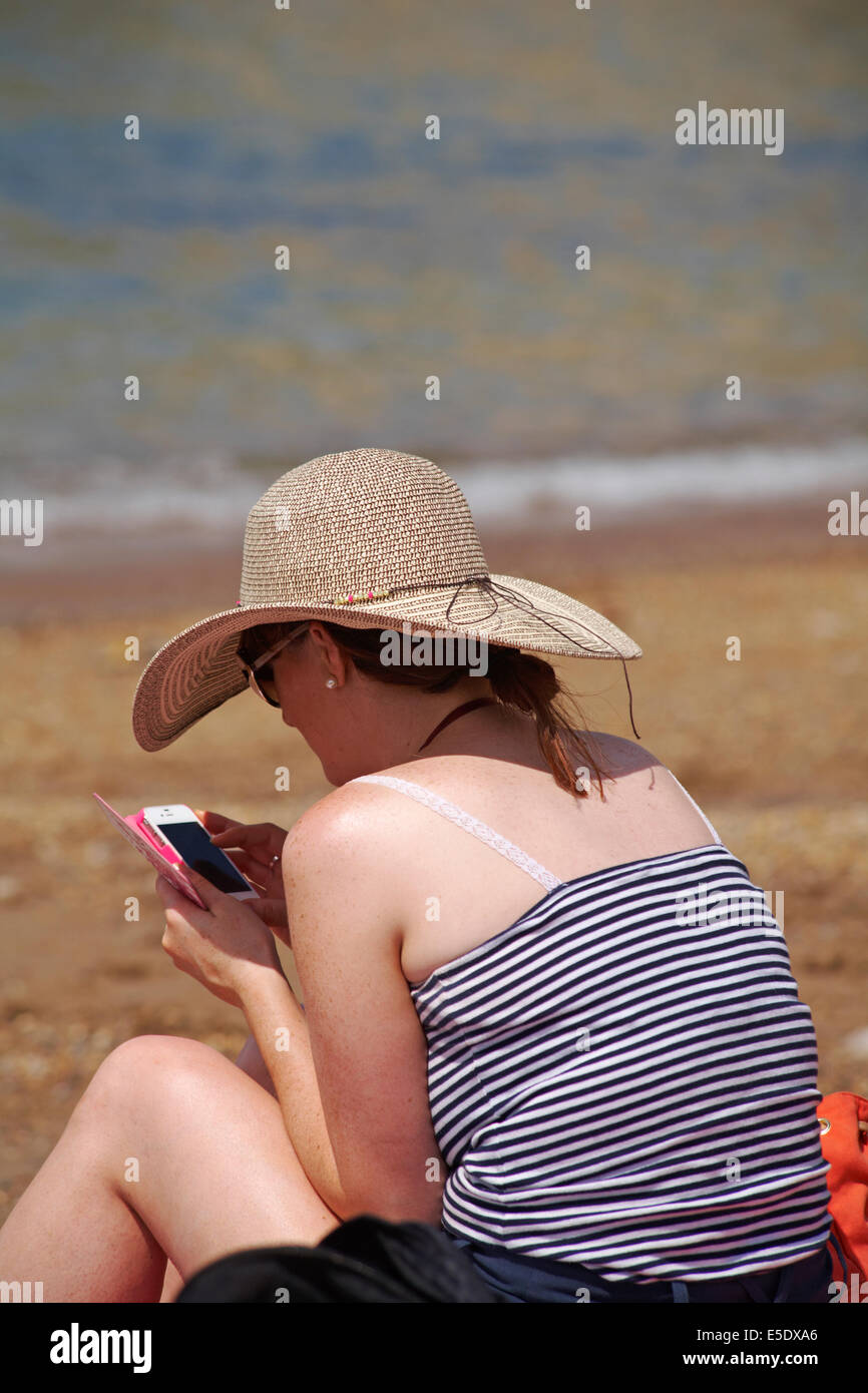 Donna che utilizza il telefono cellulare sulla spiaggia di Worbarrow Bay, Isle of Purbeck, Dorset in luglio Foto Stock