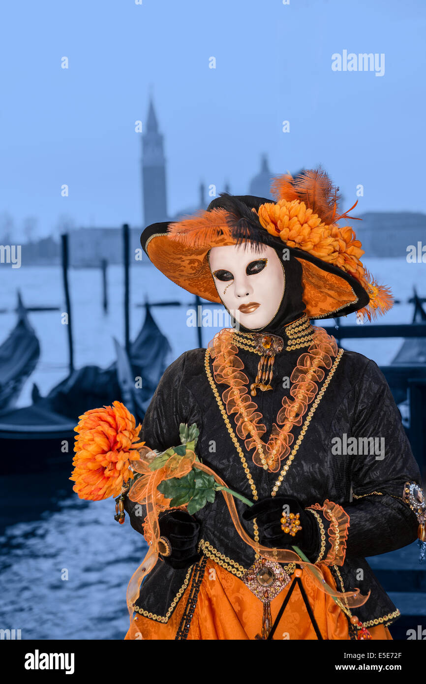 La donna a elaborare in arancione e nero costume di carnevale con fiori arancione in gondola sul lungomare di Venezia. Foto Stock
