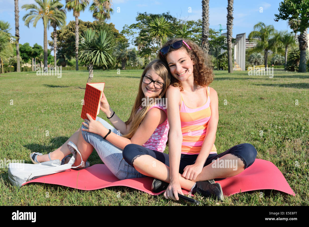 Due ragazza goofing intorno e leggere su un prato in posizione di parcheggio Foto Stock