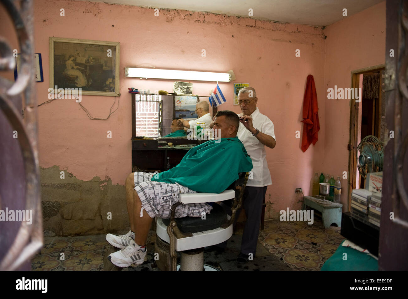 Un barbiere tagli di capelli i clienti nel suo negozio di barbiere eseguito al di fuori della propria casa nel centro di Havana, Cuba. Foto Stock