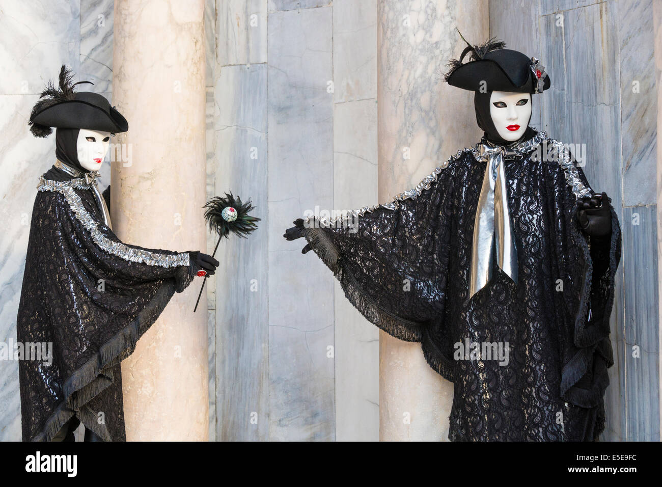 Due uomini in costumi di fantasia di nero e argento hand off una bacchetta sfumato al di fuori Cattedrale di San Marco durante il Carnevale di Venezia. Foto Stock