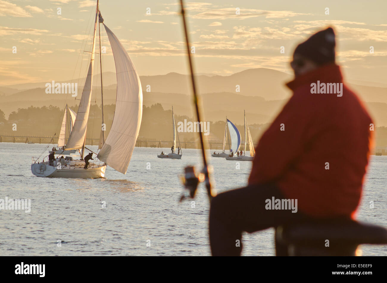 Barche a vela e il pescatore al tramonto sulla baia di Santander. Foto Stock