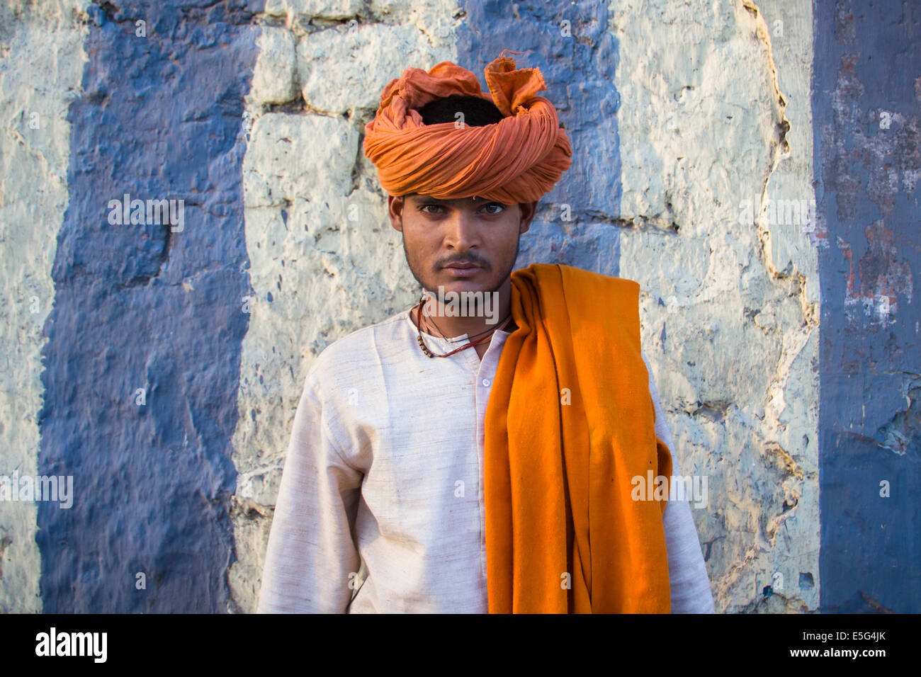Giovani colorato uomo indù, indossando un turban arancione, posa davanti un muro a strisce nella parte vecchia di Nuova Delhi, capitale dell'India. Foto Stock