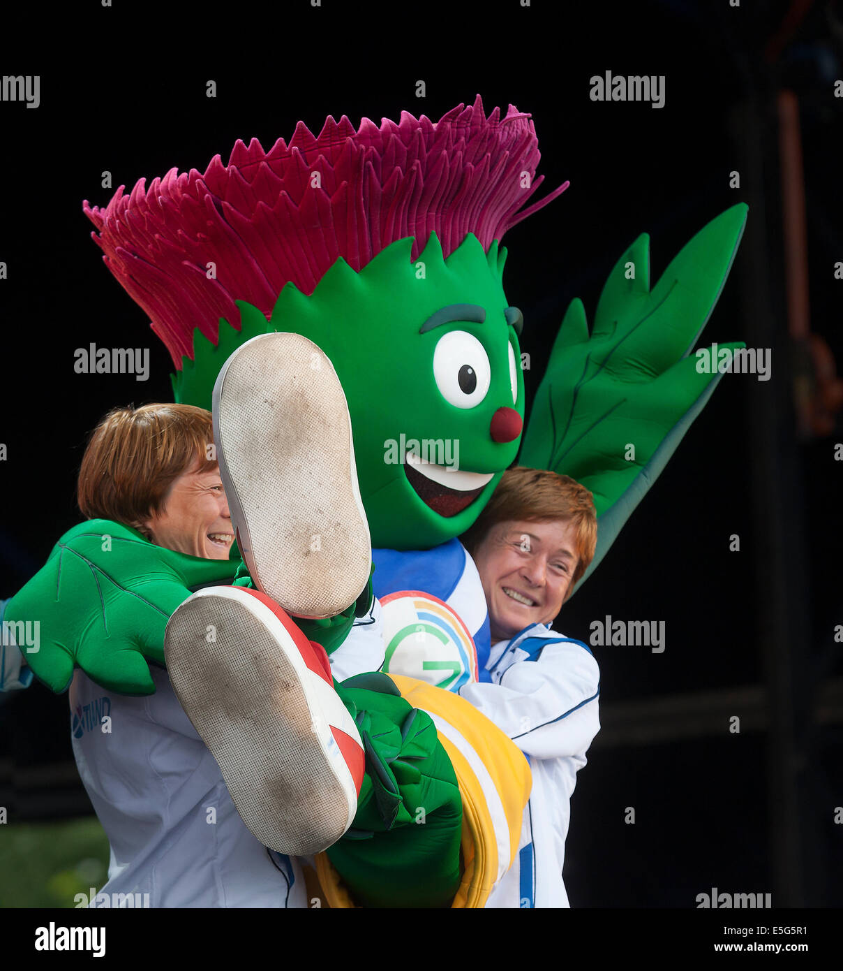 Glasgow, Scotland, Regno Unito. Il 30 luglio, 2014. Donna e Fiona Robertson, twin lottatori, sollevamento Clyde, i giochi del Commonwealth Glasgow 2014 mascotte, sul palco a Glasgow Green durante il Festival 2014, un festival culturale in parallelo con i giochi in Glasgow. Foto Stock