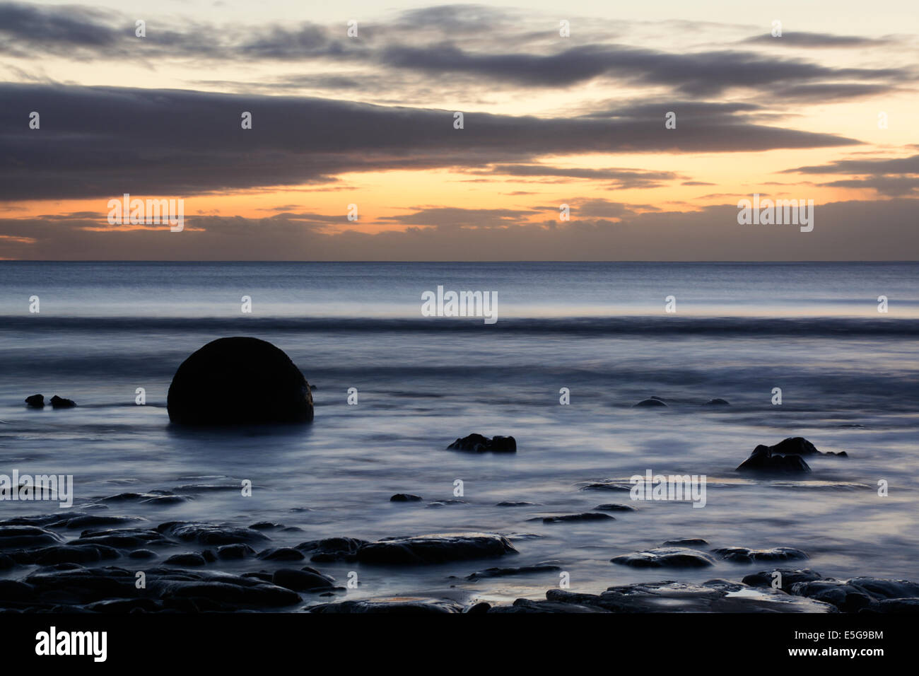 Alba sul Koekohe Beach con un masso Moeraki Foto Stock