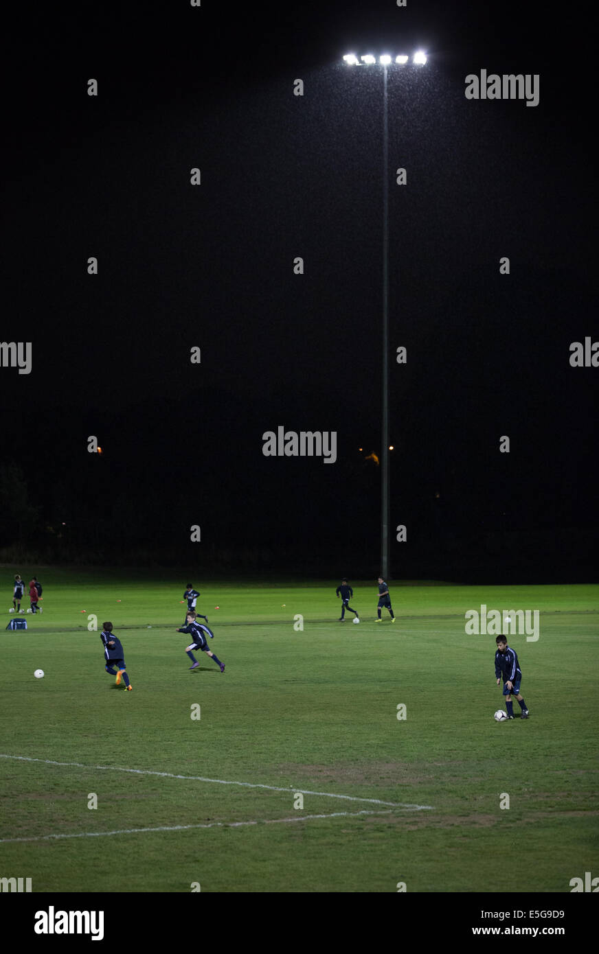 I bambini che giocano a calcio sotto i proiettori Foto Stock