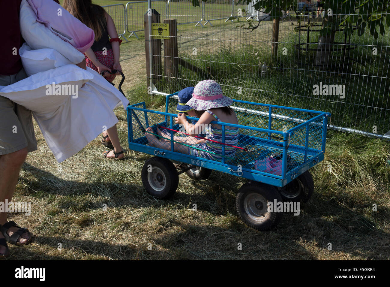 Madre tirando i bambini in un carrello. Campeggio a una festa di famiglia. Uomo che porta biancheria da letto. Cuscini. Foto Stock
