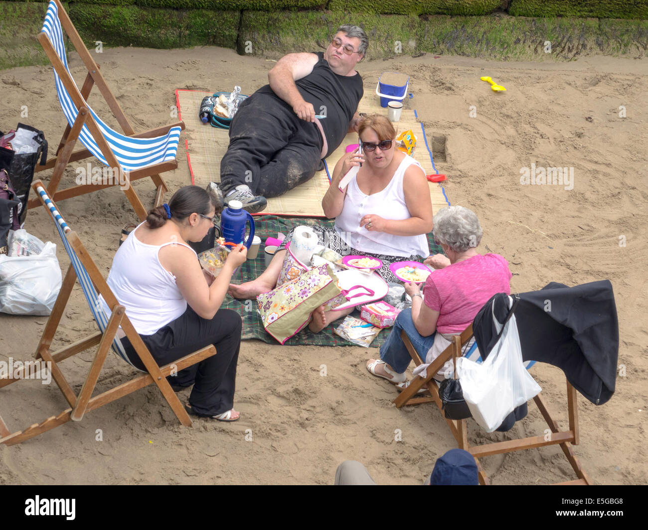 Di mezza età gruppo di famiglia godendo di un picnic su un angolo riparato di Whitby west beach Foto Stock