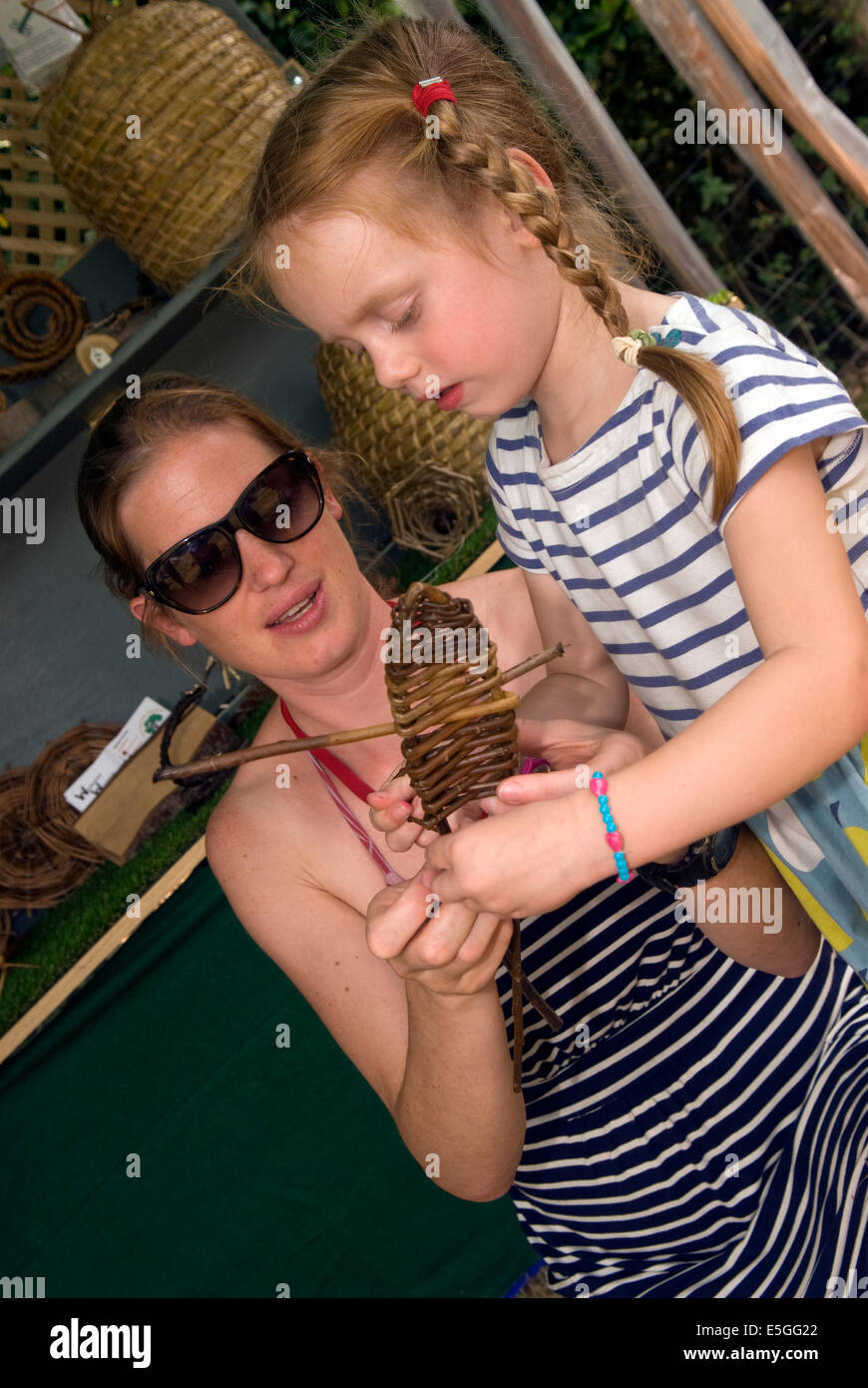 Madre con sua figlia di 4 anni la tessitura di una willow pesce in un paese artigianato giorno, Haslemere, Surrey, Regno Unito. Foto Stock