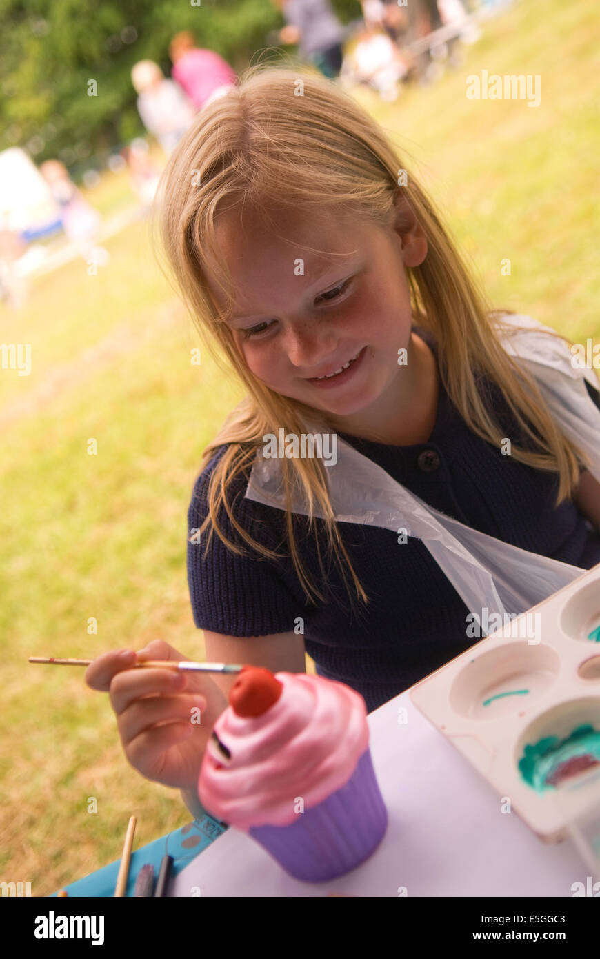 6 anno vecchia ragazza di verniciatura di un cup cake a una comunità locale giornata di divertimento, Bordon, hampshire, Regno Unito. Foto Stock