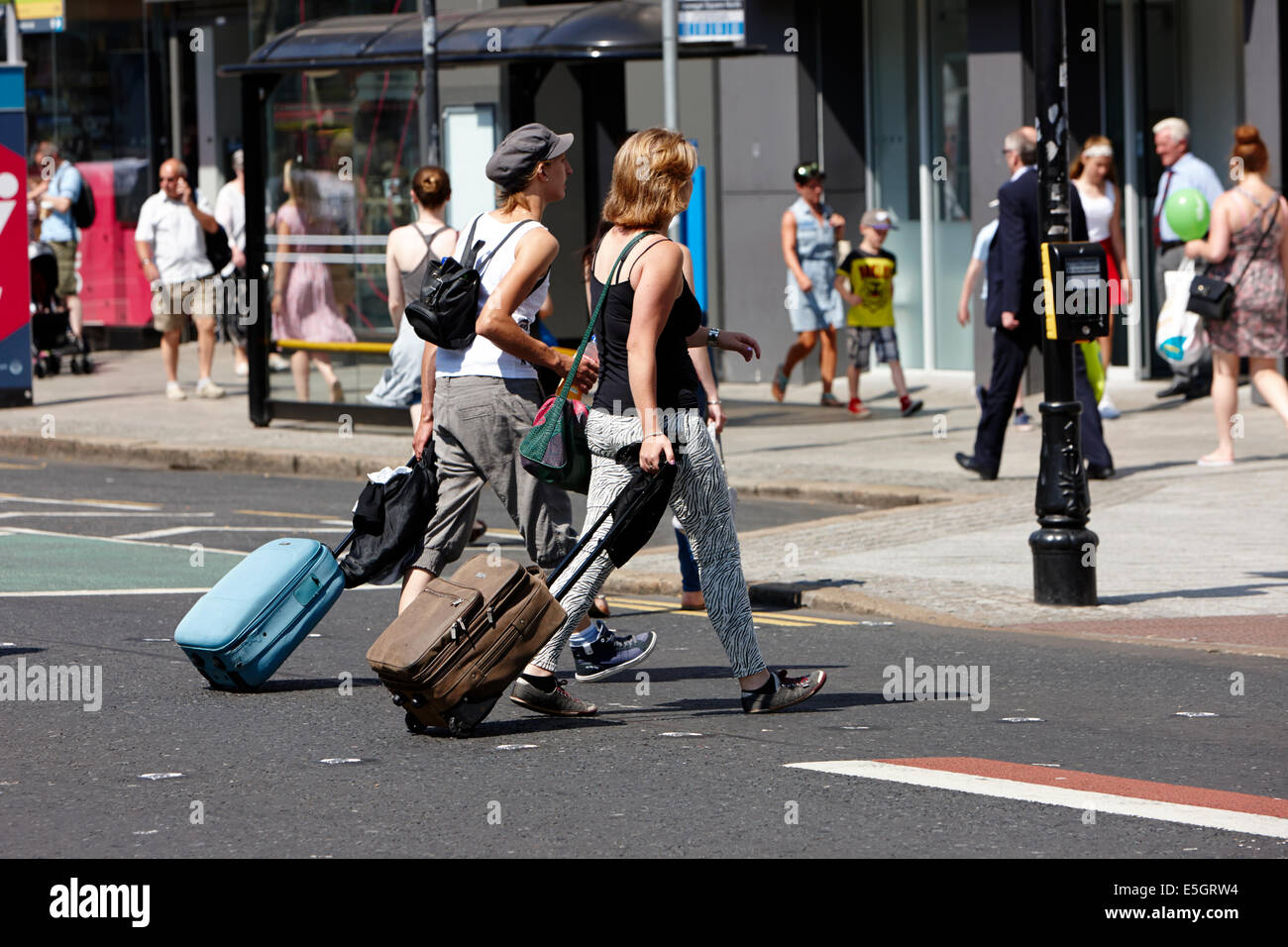 Due donne con la valigia con ruote a piedi attraverso la strada in Belfast City Centre Foto Stock