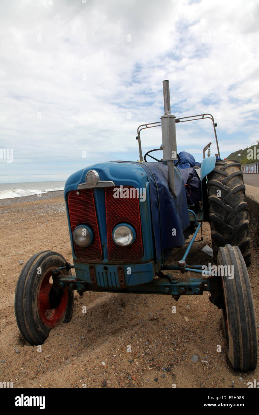 Un antico trattore su una spiaggia di Norfolk, utilizzato per tirare le barche per la pesca in acqua e fuori Foto Stock