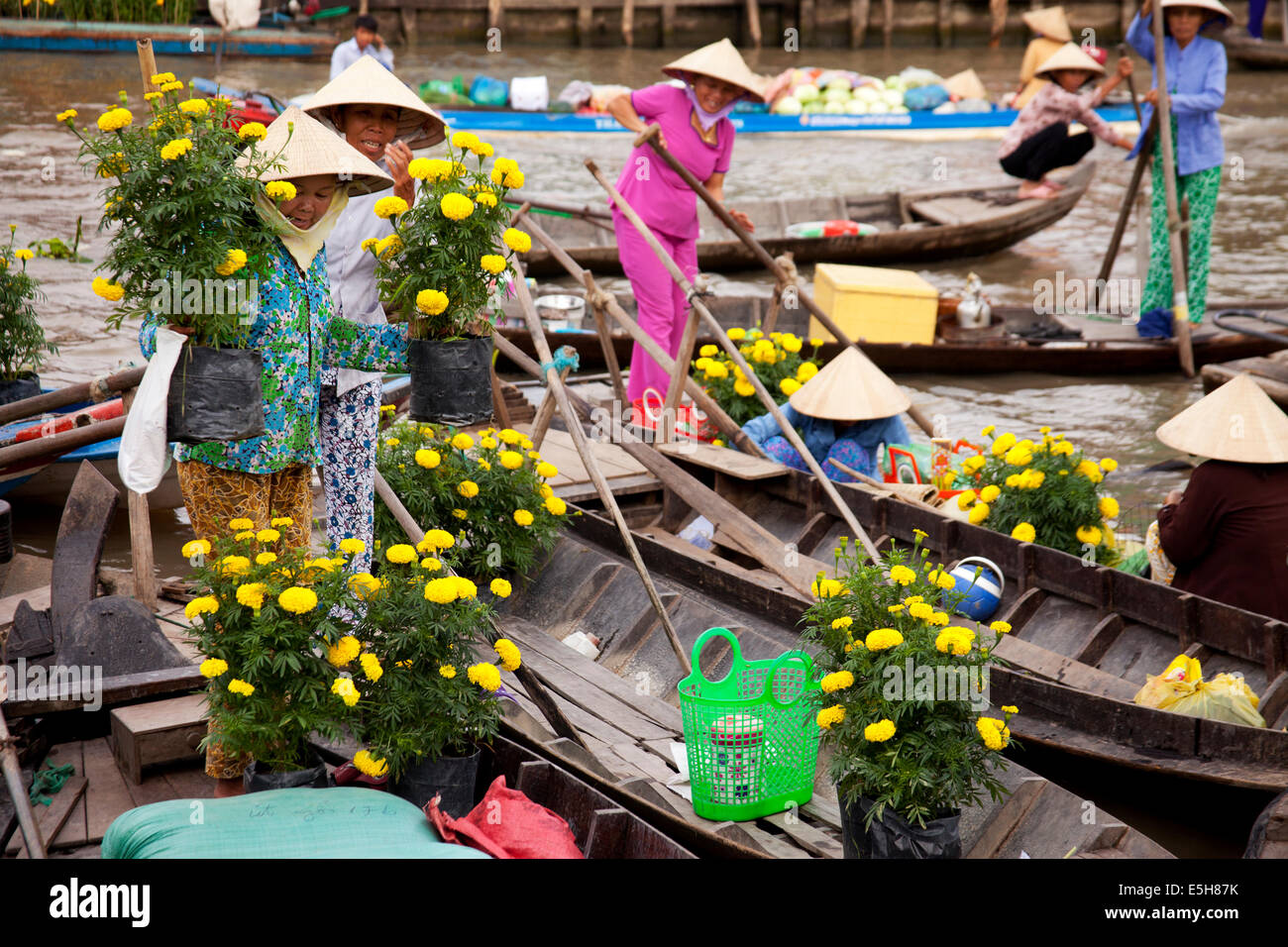 Donne che indossano cappelli conici scaricare fiori gialli da una barca nel mercato galleggiante nella Soc Trang, una città del Delta del Mekong. Foto Stock