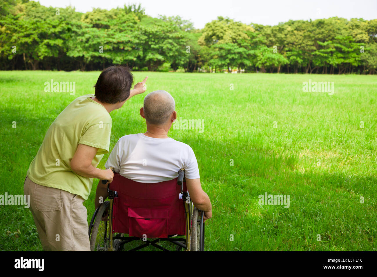 Senior uomo seduto su una sedia a rotelle con sua moglie Foto Stock