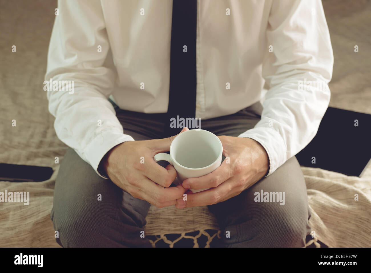 Imprenditore solitario nella camera di albergo di seduta sul letto e tenendo tazza vuota Foto Stock