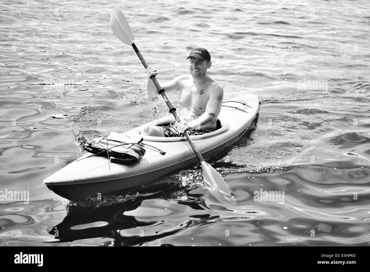 Uomo che indossa un cappello da baseball in kayak sulle acque in BW Foto Stock