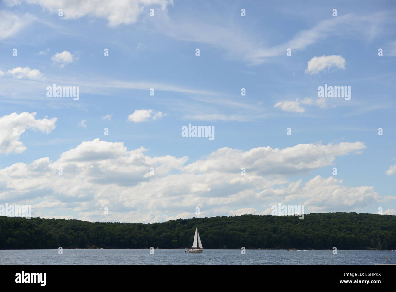 Barca a vela sul lago con le montagne e un bel cielo blu con il bianco puffy nuvole Foto Stock
