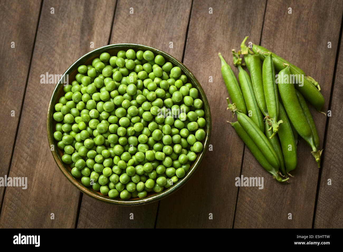 Piselli (lat. Pisum sativum) nella ciotola con peapods chiusa sul lato Foto Stock