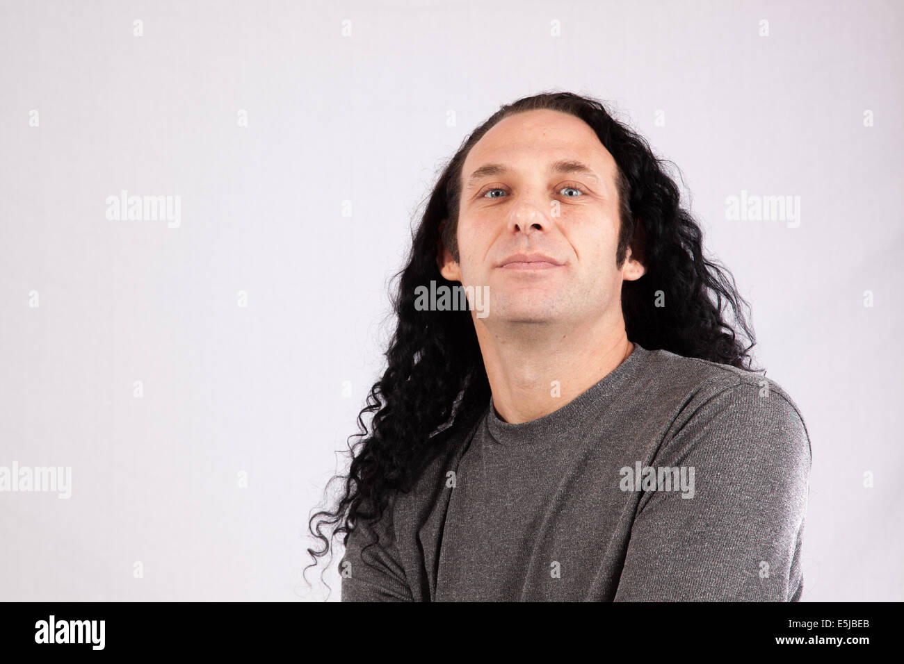 Maschio caucasico con i capelli lunghi e la camicia grigia guardando pensieroso Foto Stock