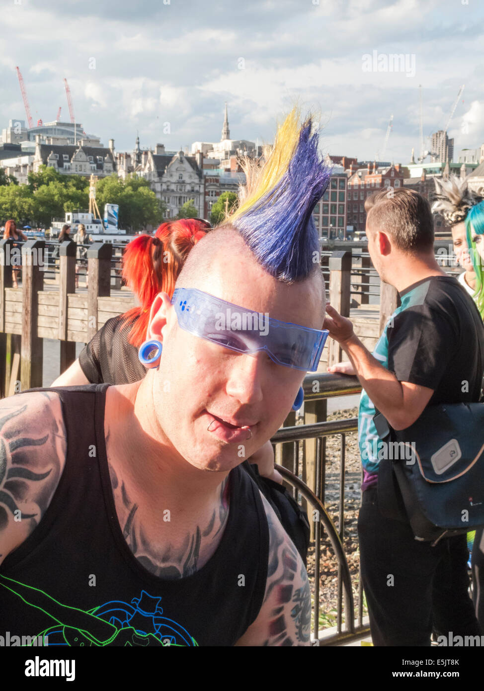 Lo stile di vita moderno: un giovane uomo con i tatuaggi, labbro piercing e un multi-gel colorato mohicano punk acconciatura e cool blue occhiali da sole, South Bank di Londra Foto Stock
