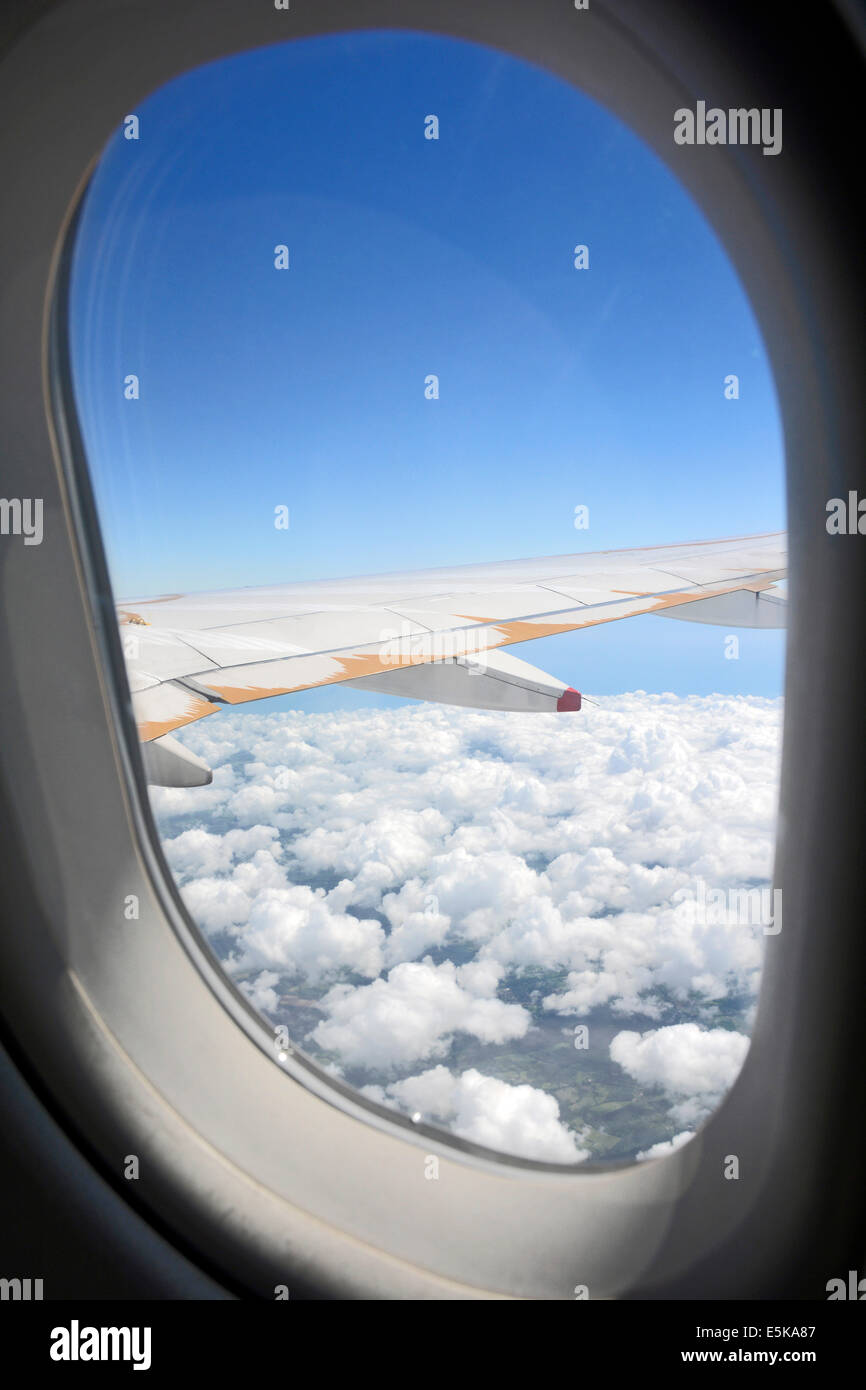 Vista passeggeri di aereo sul telaio di una finestra e un'ala di un velivolo con il bianco delle nuvole e un cielo blu battenti in Europa Foto Stock