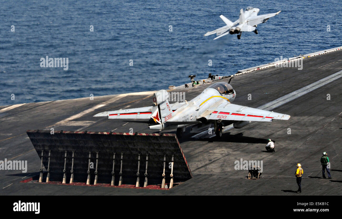 Un US Navy F/A-18F Super Hornet fighter aircraft gira a sinistra come marinai preparare per il lancio di un EA-6B Prowler aerei off il ponte di volo della portaerei USS George H.W. Bush Luglio 1, 2014 in mare Arabico. Foto Stock