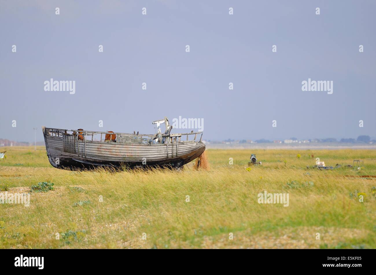 Abbandonato derelitto barca di pesca trascinato su l'erba coperta ghiaia riva sopra l'acqua alta. Dungeness, Kent, Inghilterra, Regno Unito. Foto Stock