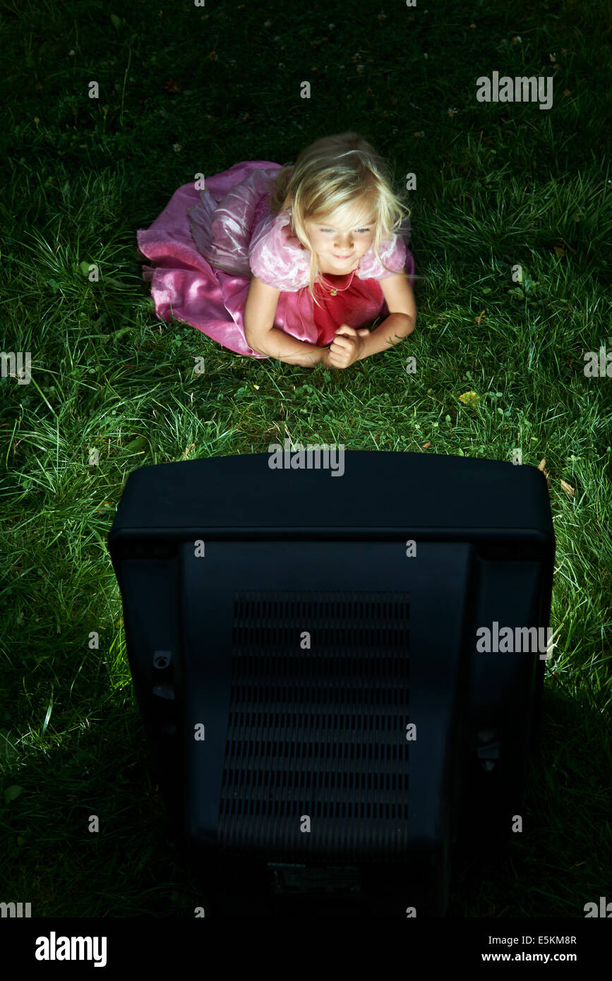 Bambino ragazza bionda vestita come la principessa guardando la vecchia televisione al di fuori nel prato verde cortile Foto Stock