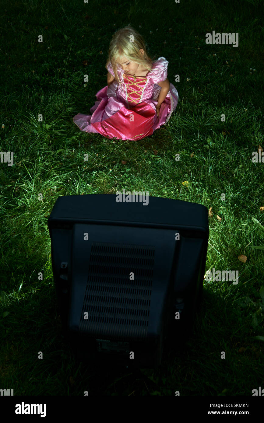 Bambino ragazza bionda vestita come la principessa guardando la vecchia televisione al di fuori nel prato verde cortile Foto Stock