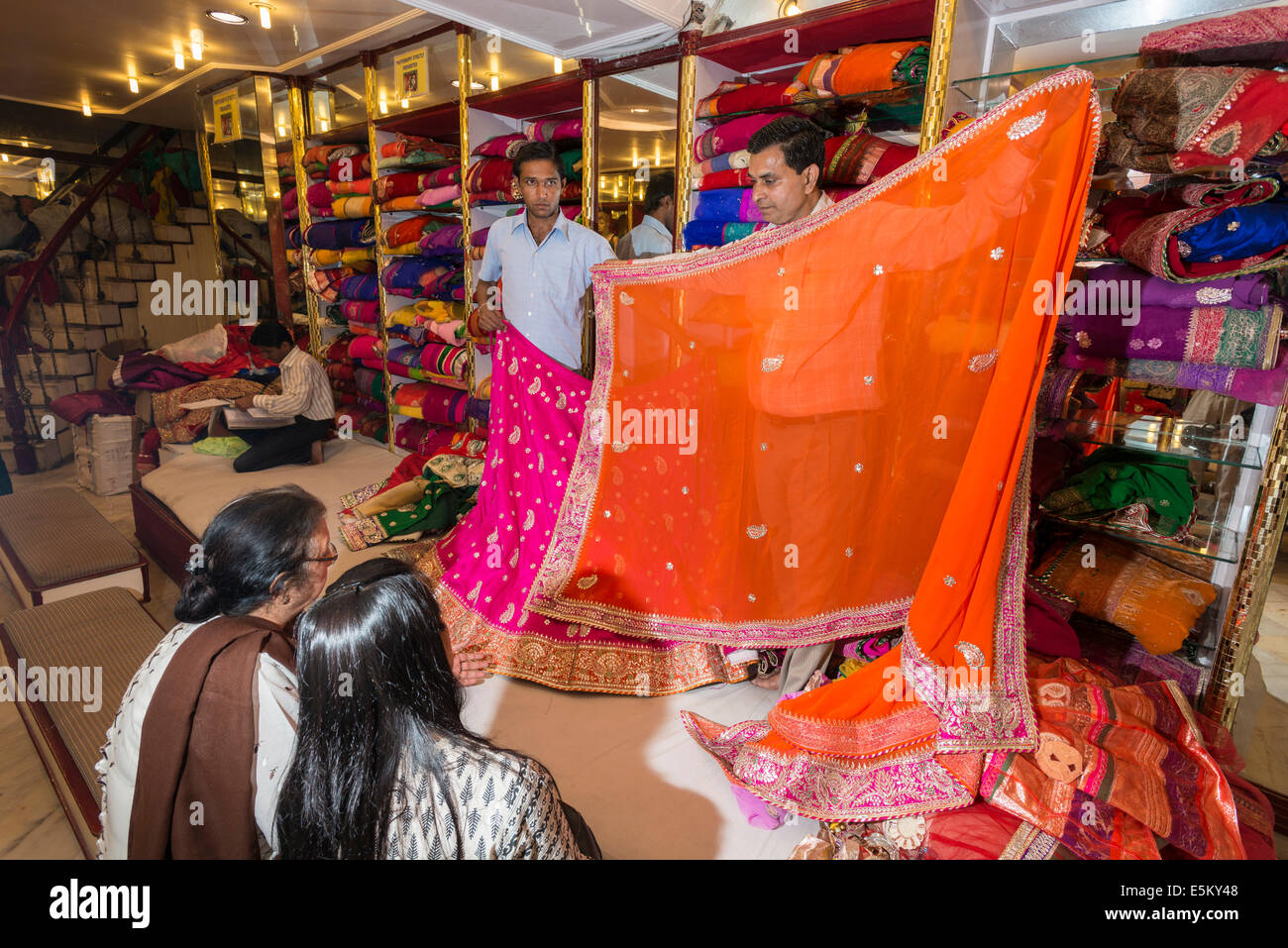 Shop assistenti presentando sari colorati ai clienti, Jaipur, Rajasthan, India Foto Stock