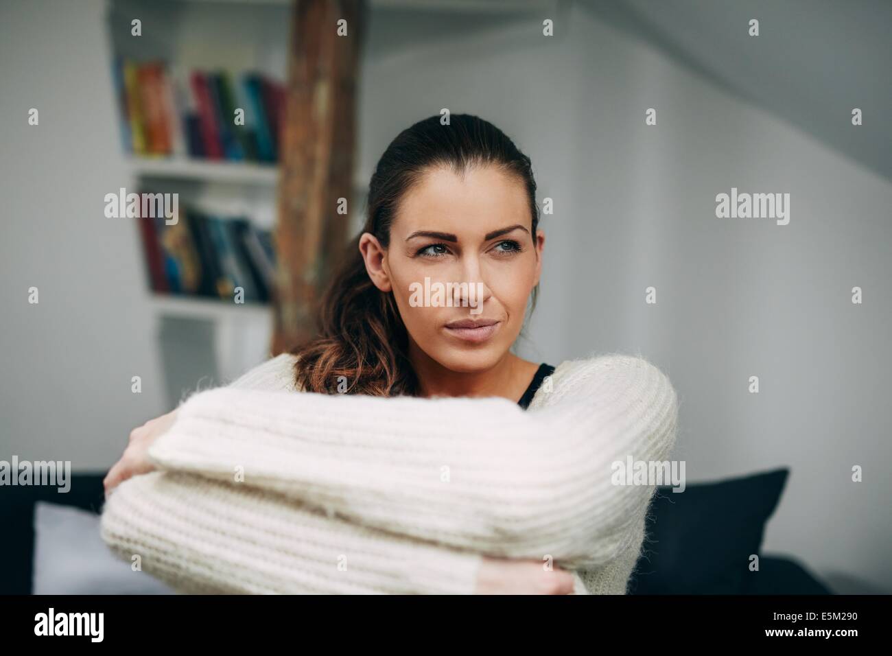 Ritratto di giovane donna sola seduta sul divano guardando lontano. Caucasian modello femminile a casa fantasticando. Foto Stock