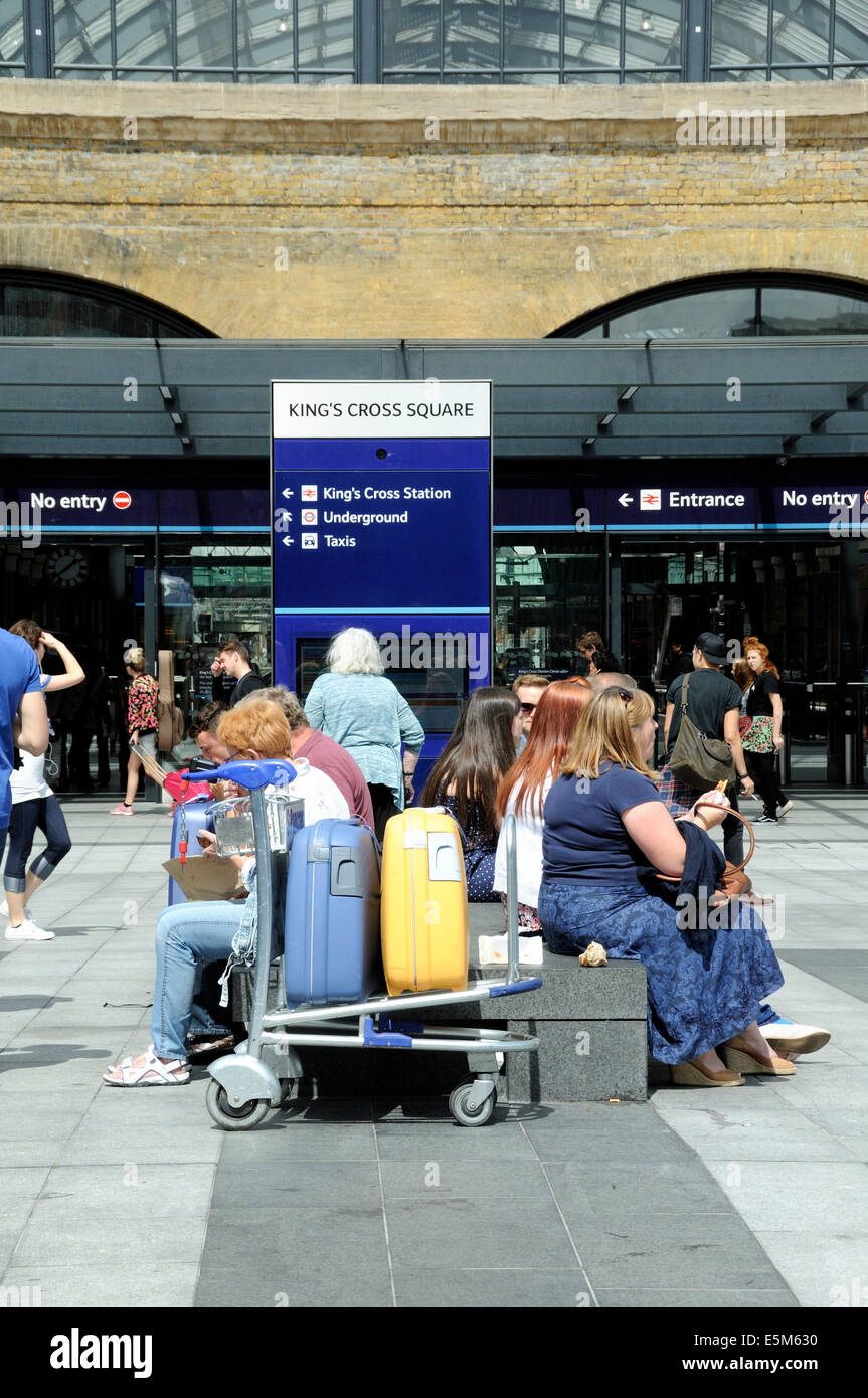 La gente seduta in Kings Cross Station Square con i bagagli, Londra Inghilterra Gran Bretagna REGNO UNITO Foto Stock
