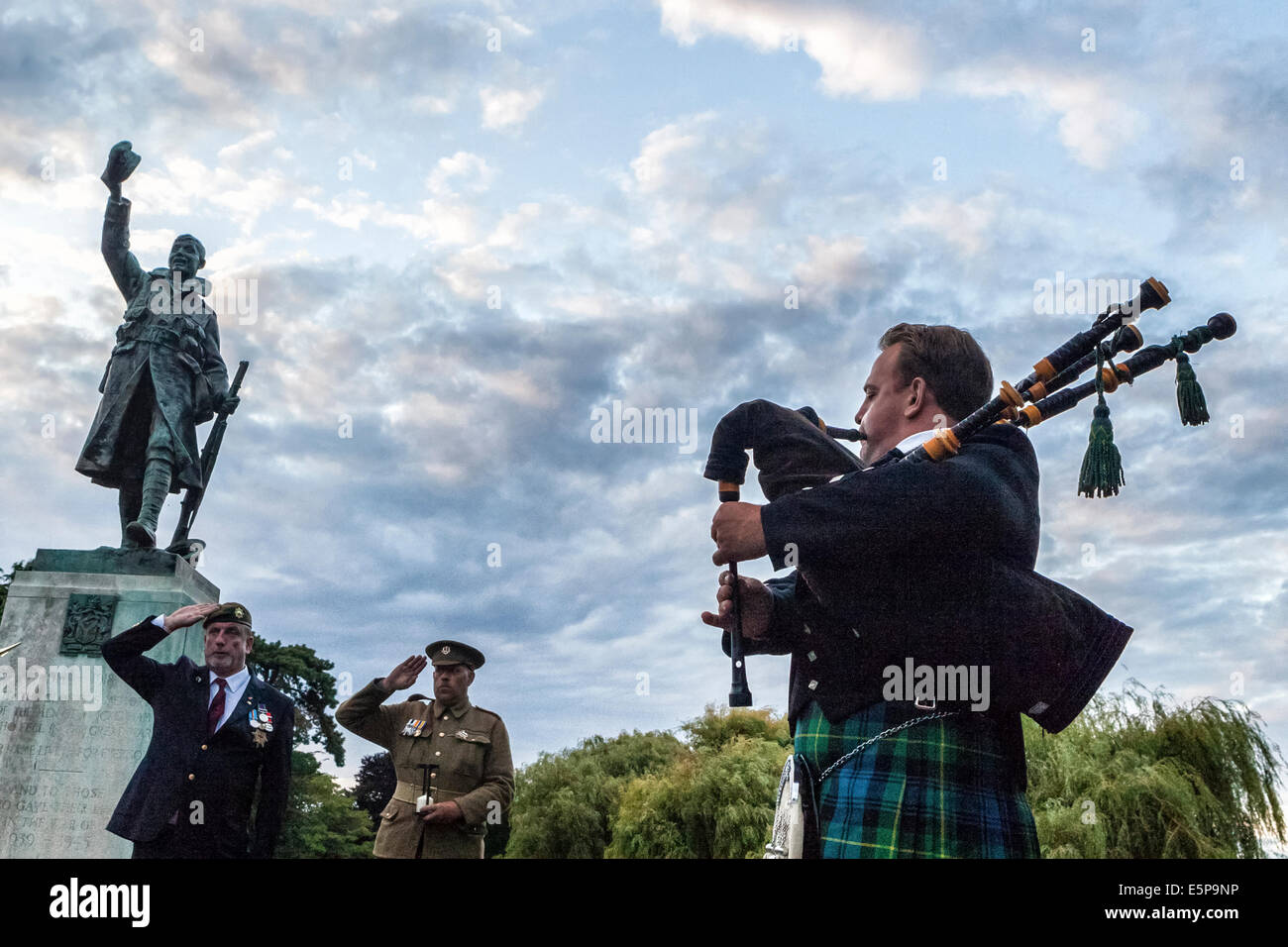 UK, Londra, Twickenham, Radnor Giardini, 4° agosto 2014. Un lone piper accompagnatrici standard per il memoriale di guerra durante una veglia per commemorare la dichiarazione di guerra il 4 agosto 1914. La veglia è stato frequentato dal sindaco del London Borough of Richmond upon Thames, Assessore Jane Boulton, e la Sua Altezza Serenissima Principessa Marie-Therese von HohenBerg, Onorevole Anthony Bailey e il sig. Anthony Bailey OBE GCSS. Il pubblico sono stati invitati a un tramonto servizio commemorativo condotto da Padre David Loftus MBE. Credito: Eden Breitz/Alamy Live News Foto Stock