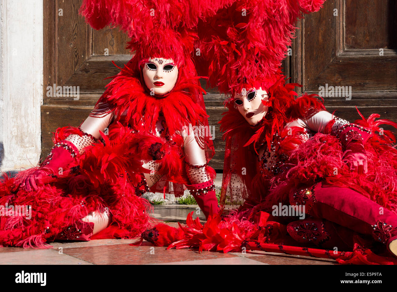 Coppia di donne in rosso elaborati costumi sfumato reclino nella parte anteriore della porta della chiesa di san Zaccaria durante il carnevale di Venezia. Foto Stock