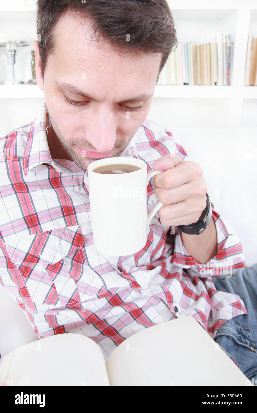 Uomo informale di bere il caffè o il tè e la lettura di libro in un momento di relax a casa Foto Stock