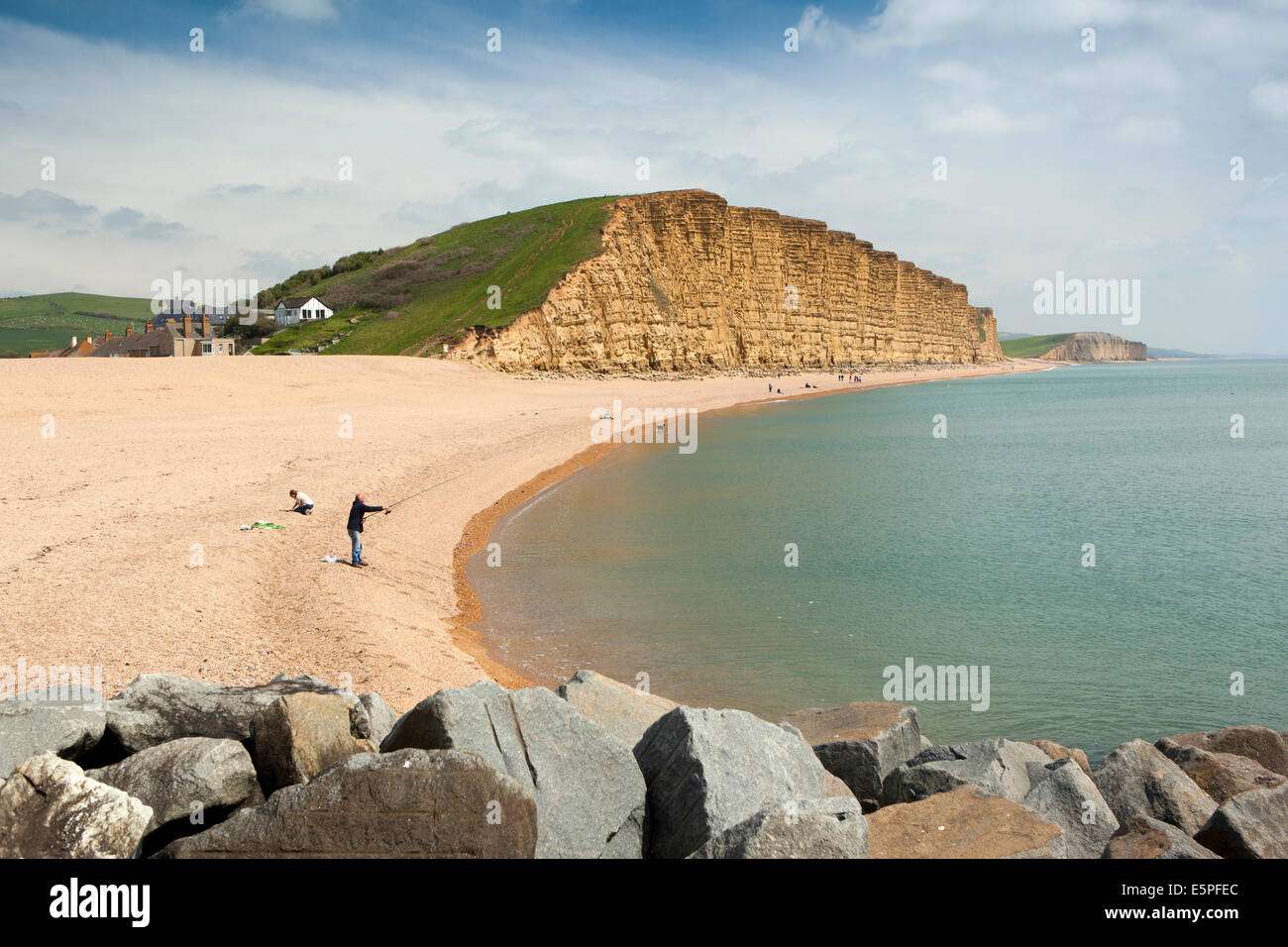 Regno Unito Inghilterra, Dorset, West Bay, uomo di pesca in mare sulla spiaggia sotto le scogliere Foto Stock