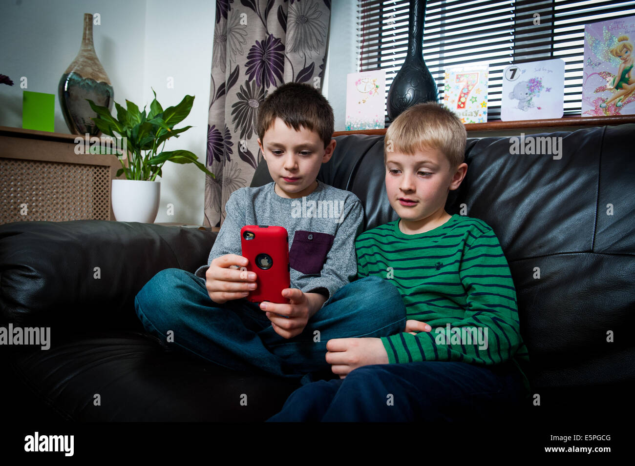 2 ragazzi 8 9 10 11 giocando a un gioco per computer sul telefono mobile,seduto sul divano Foto Stock