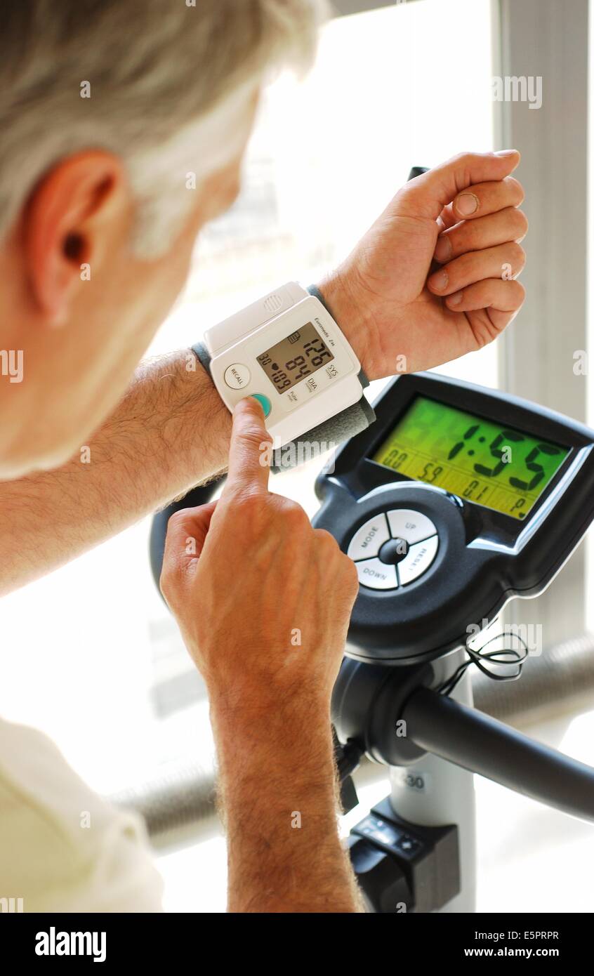 Monitoraggio uomo la sua pressione del sangue con un portatile di Sfigmomanometro digitale quando si pratica excercize bicicletta. Foto Stock