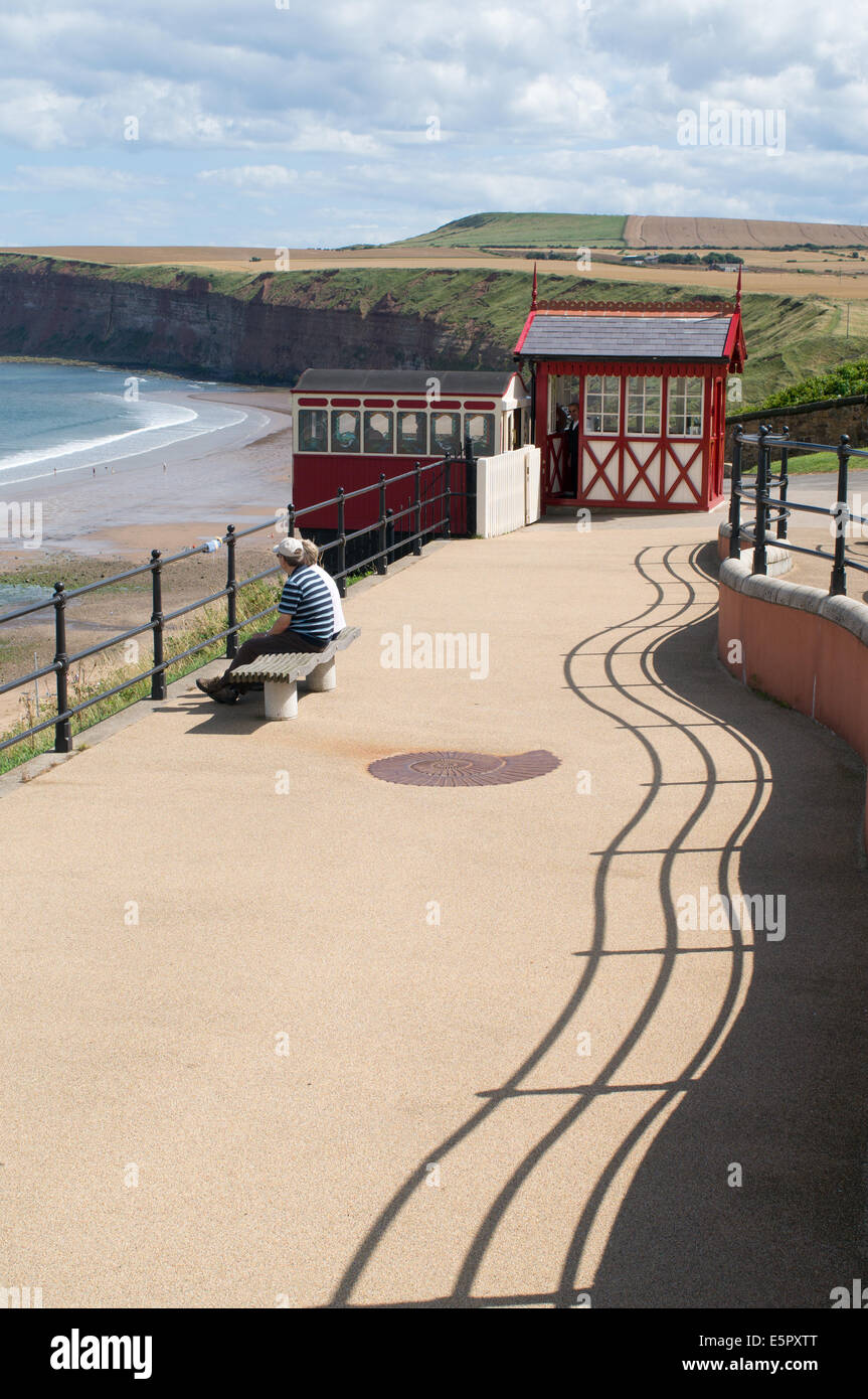 Giovane seduto che guarda al mare, con la funicolare in background, Cambs, Redcar e Cleveland, England, Regno Unito Foto Stock