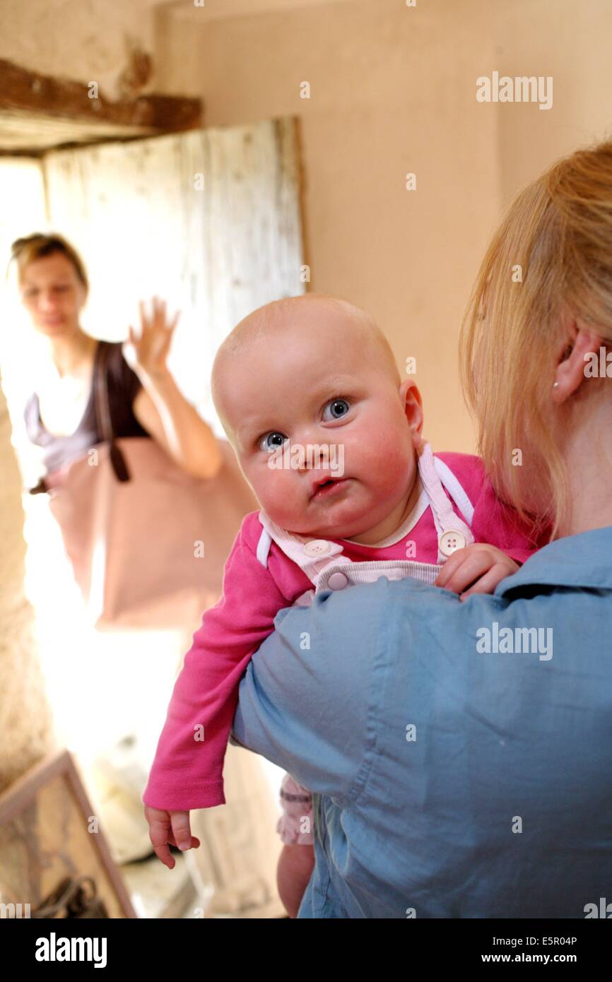 Una madre ha il suo mese 8 bambino a un operatore sanitario professionale che si prenderà cura di lui durante la sua giornata lavorativa. Foto Stock