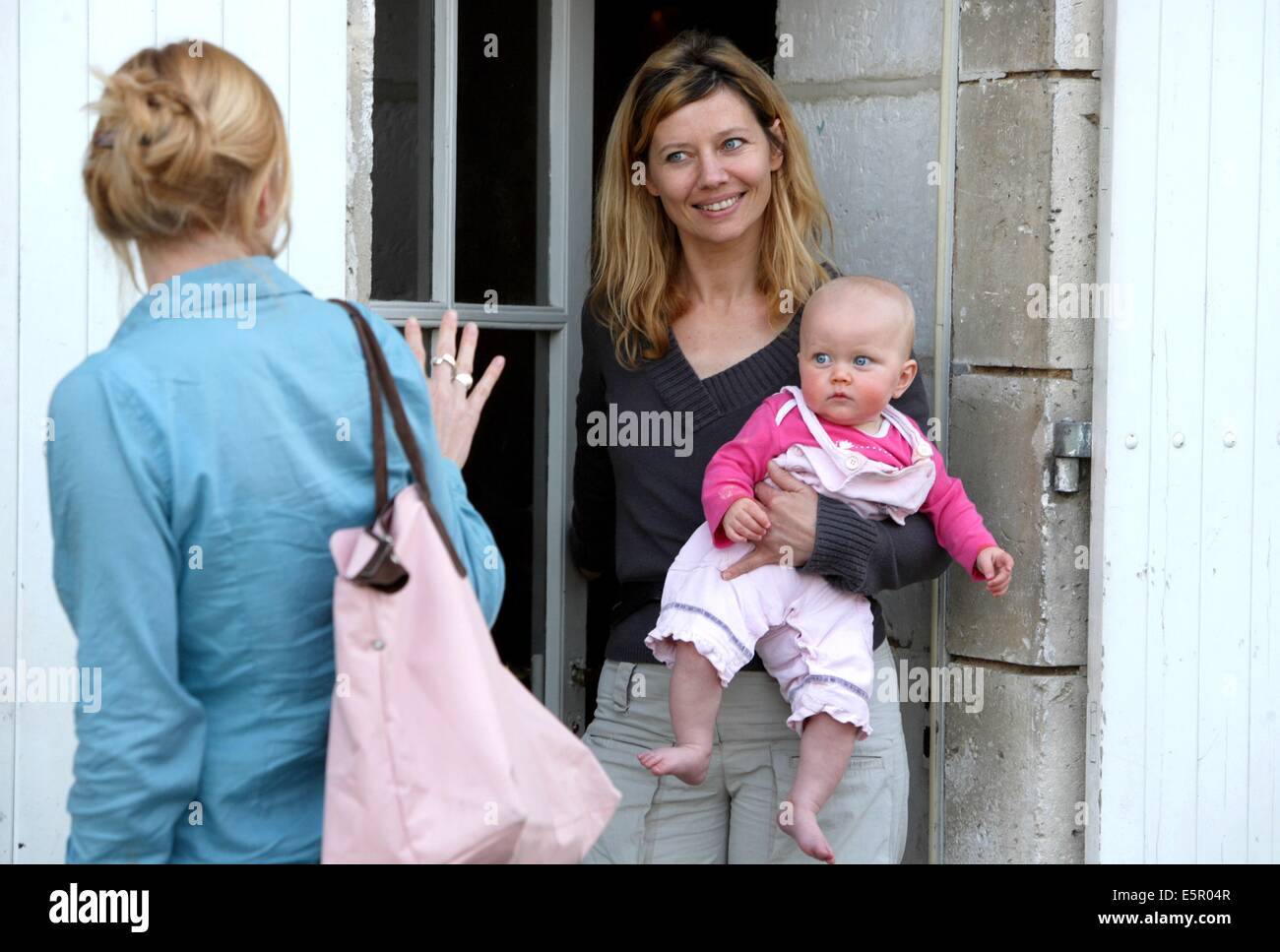 Una madre ha il suo mese 8 bambino a un operatore sanitario professionale che si prenderà cura di lui durante la sua giornata lavorativa. Foto Stock