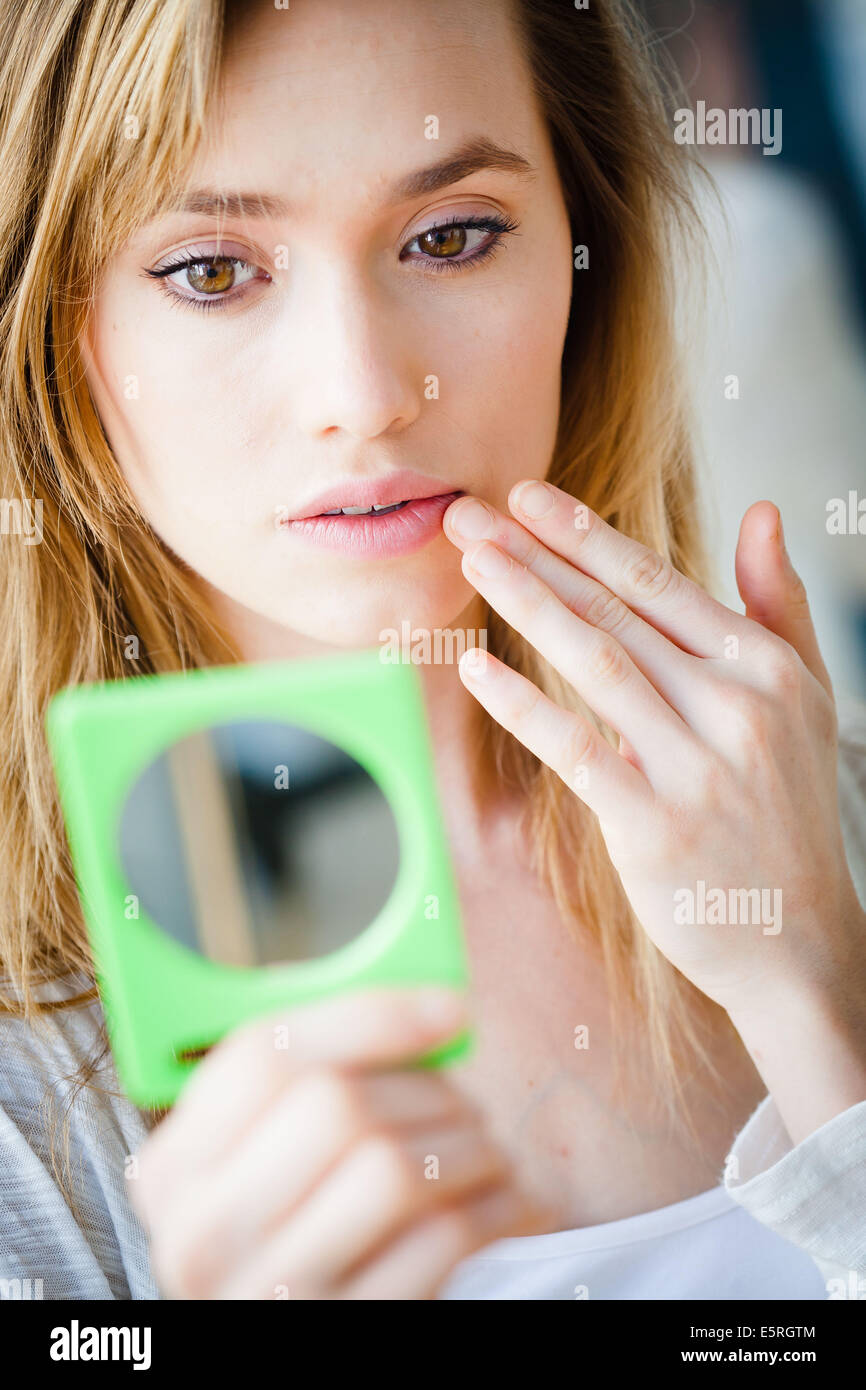 Giovane donna controllando la sua faccia nello specchio. Foto Stock