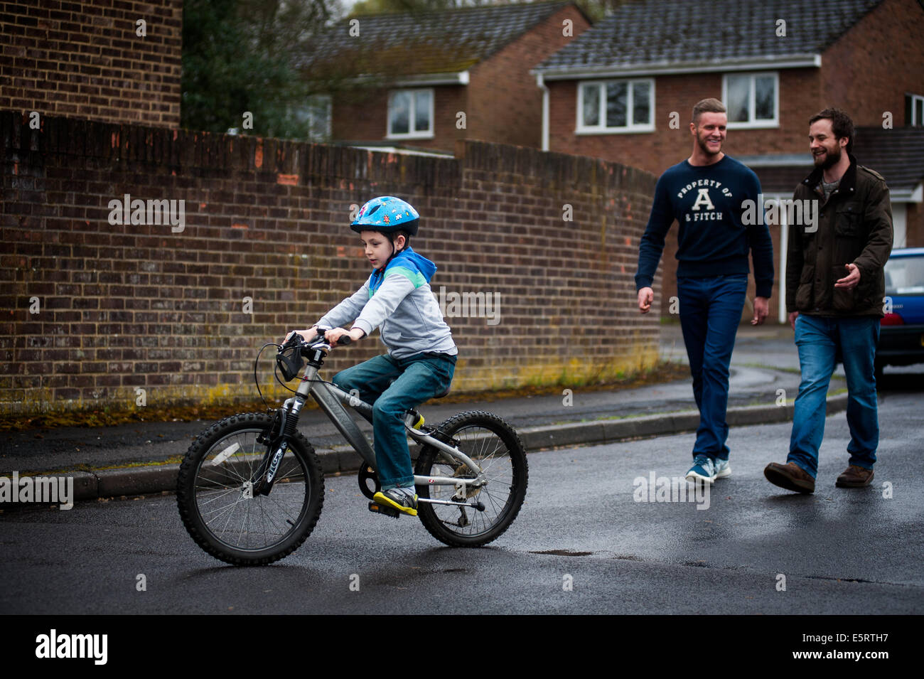 Ragazzo di imparare a correre in bici con 2 genitori maschili Foto Stock
