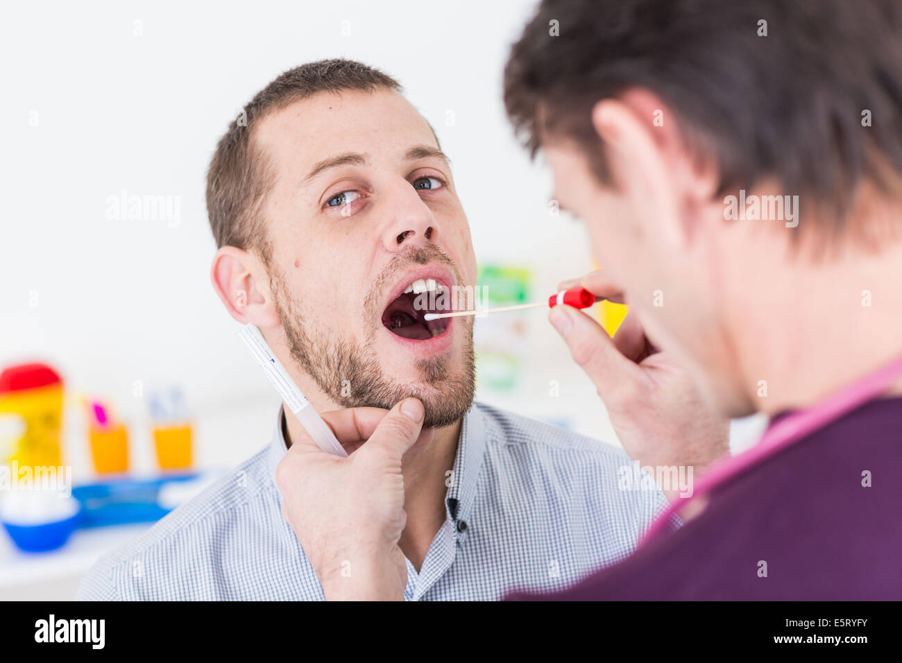 Medico usando un bastoncino di cotone per prelevare un campione da un paziente la gola del. Foto Stock