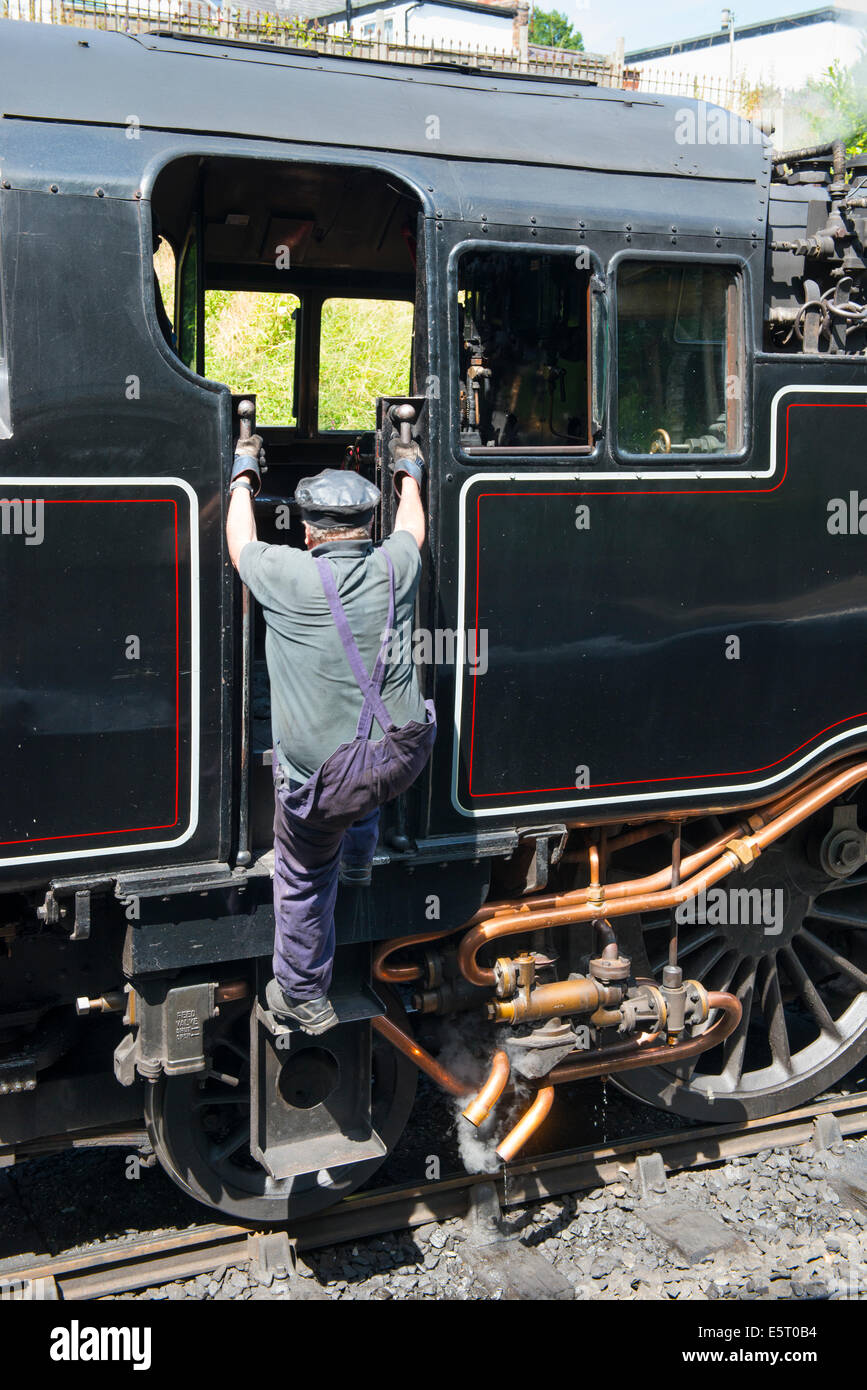 Un ingegnere arrampicate nella cabina del motore di una locomotiva a vapore a Llangollen stazione, Denbighshire, Galles. Foto Stock
