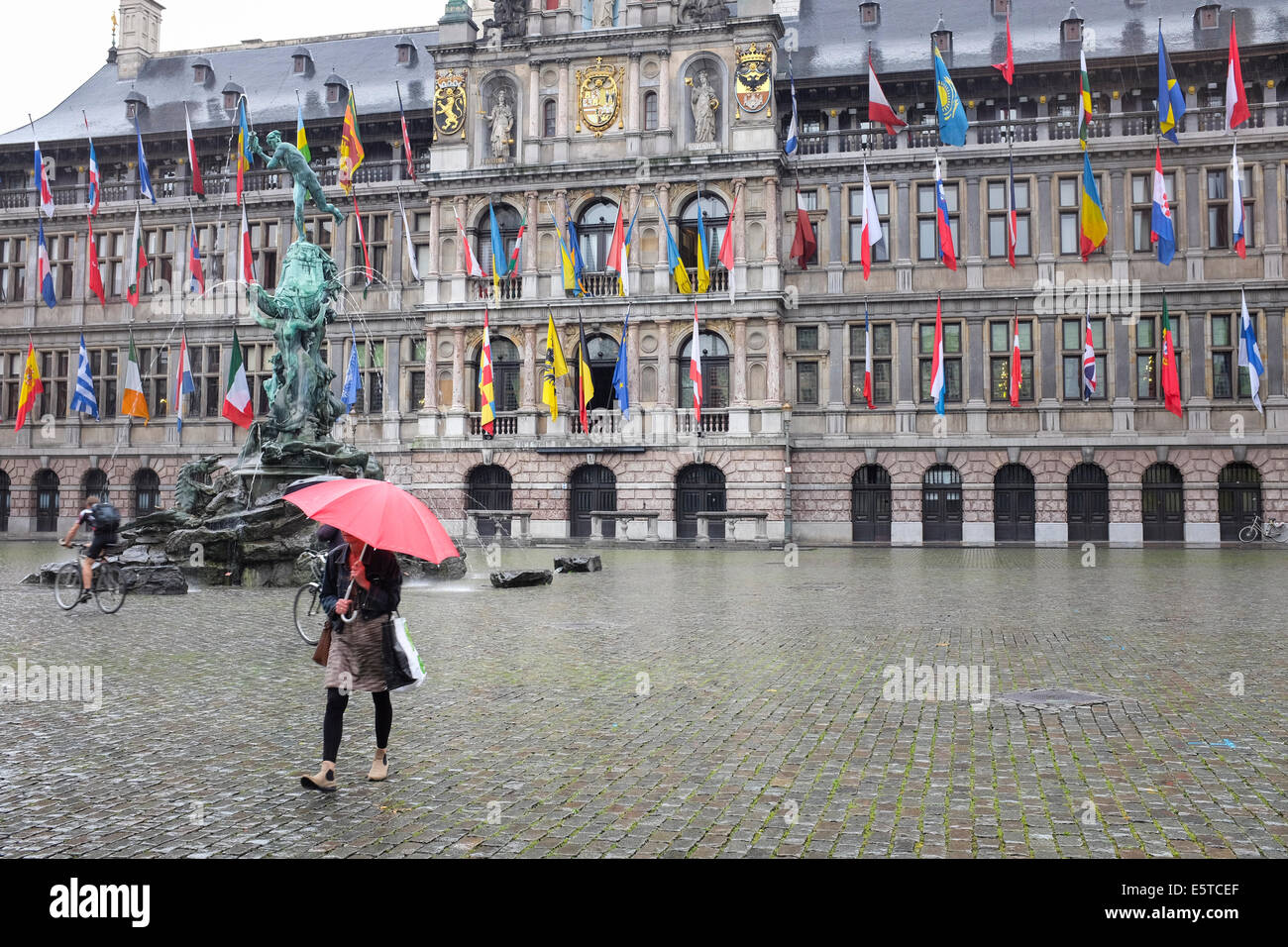 Persona a piedi sotto la pioggia nest al Municipio bandiere facciata e Brabo fontana nella città di Anversa, Belgio Foto Stock