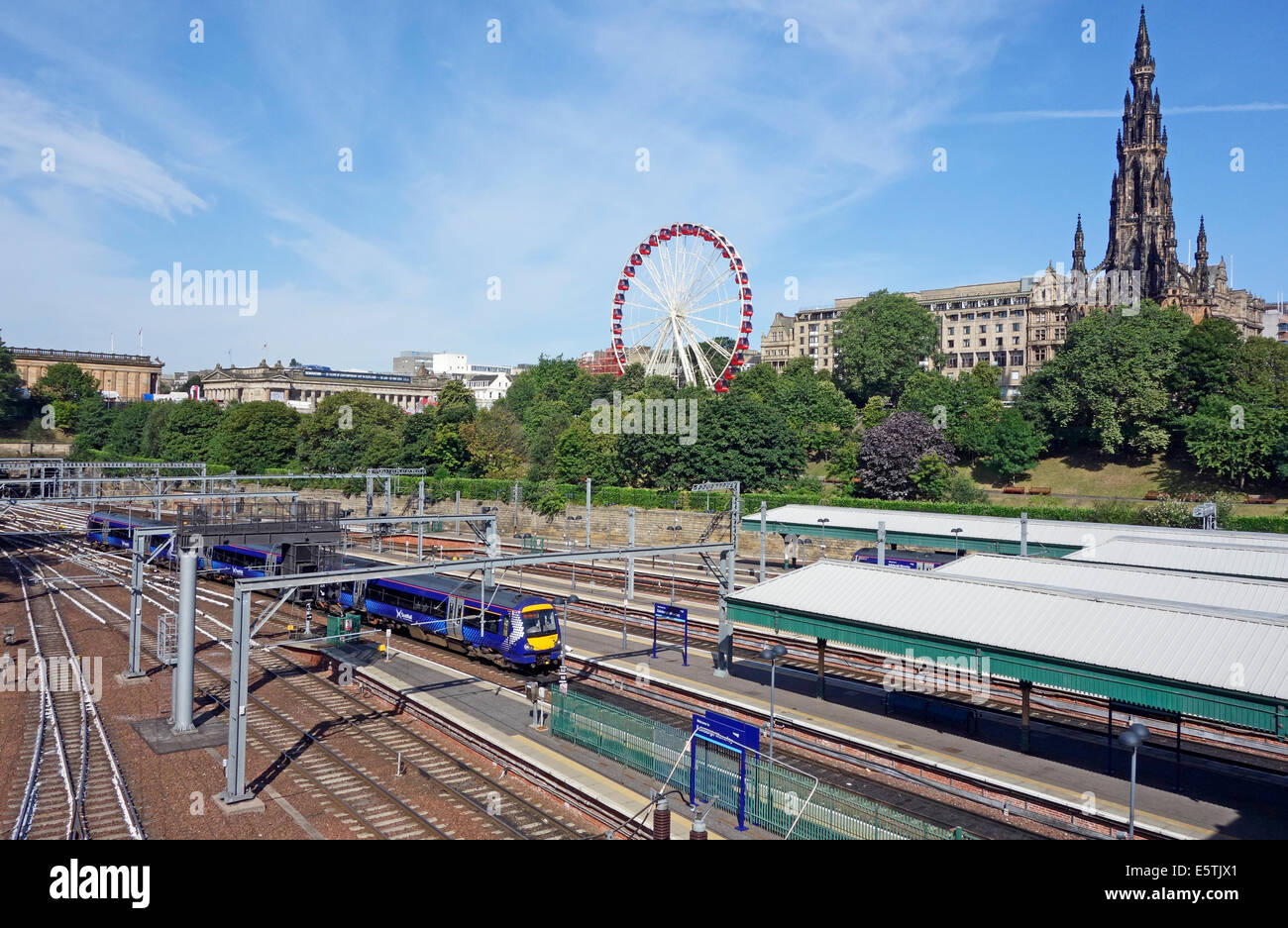 Un turbostar Scotrail treno arriva alla stazione di Waverley di Edimburgo in Scozia con la grande ruota panoramica Ferris e Monumento Scott dietro Foto Stock