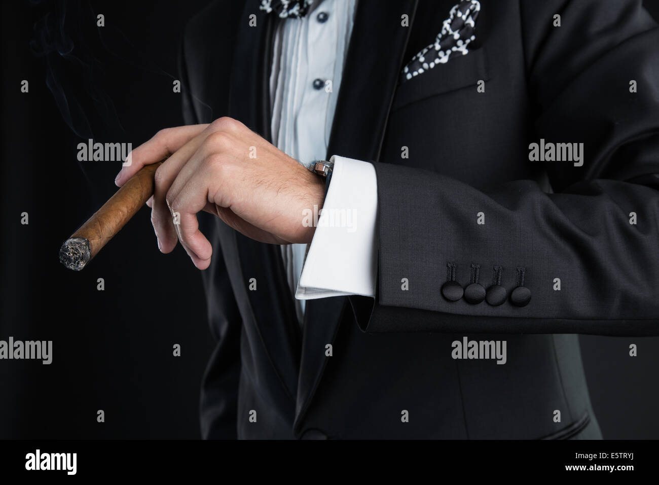 Uomo in un abito nero tenendo un sigaro in una mano sinistra Foto Stock
