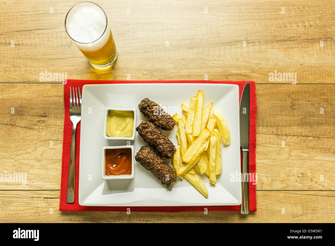 Tradizionale rumena Mici e patate fritte con ketchup, senape e bicchiere di birra Foto Stock